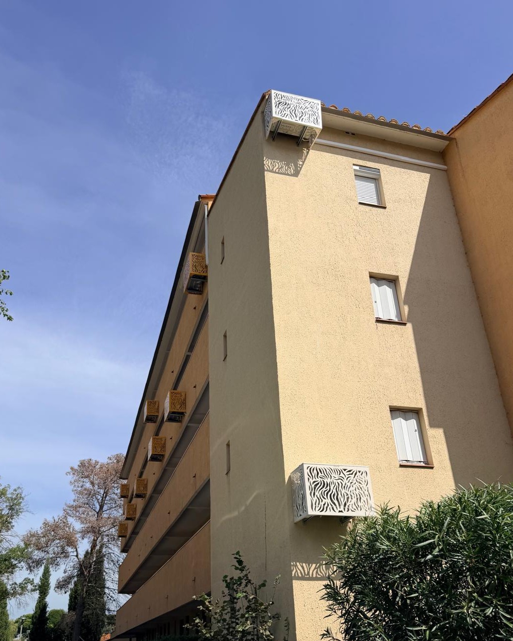 cache-clim blanc à motif installé à l'angle d'une résidence à Argelès-sur-Mer