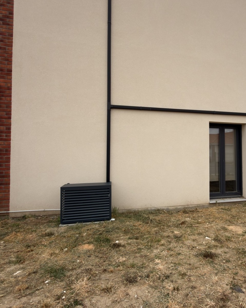 Cache clim gris anthracite habillant un groupe extérieur de climatisation contre une façade beige