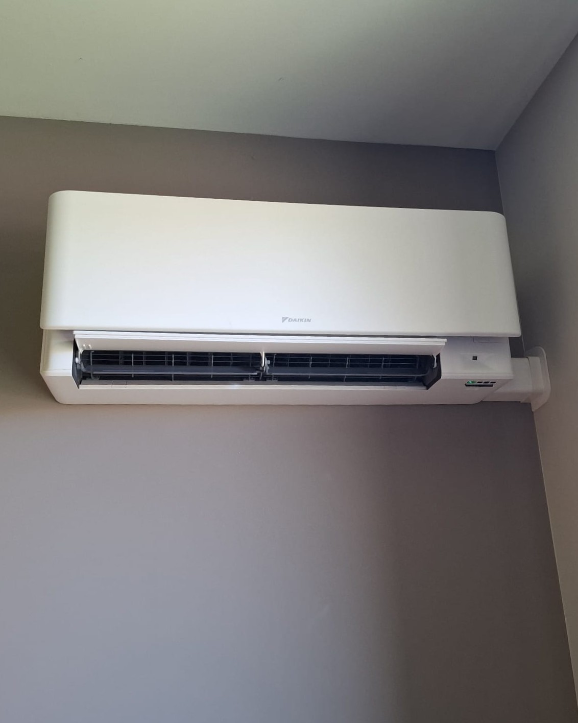 Unité murale Daikin Stylish blanche installée en hauteur dans une chambre au mur gris