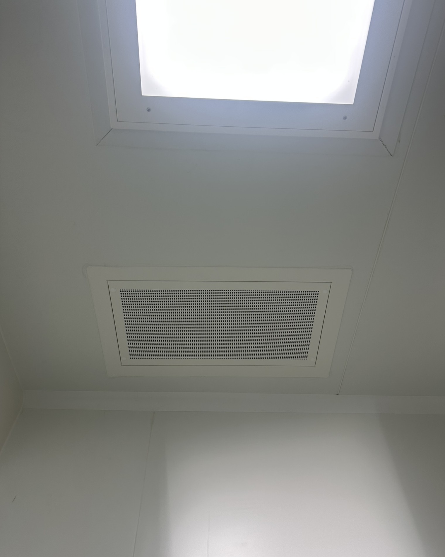 Diffuseur d'air plafonnier installé à côté d'un panneau lumineux dans une salle propre