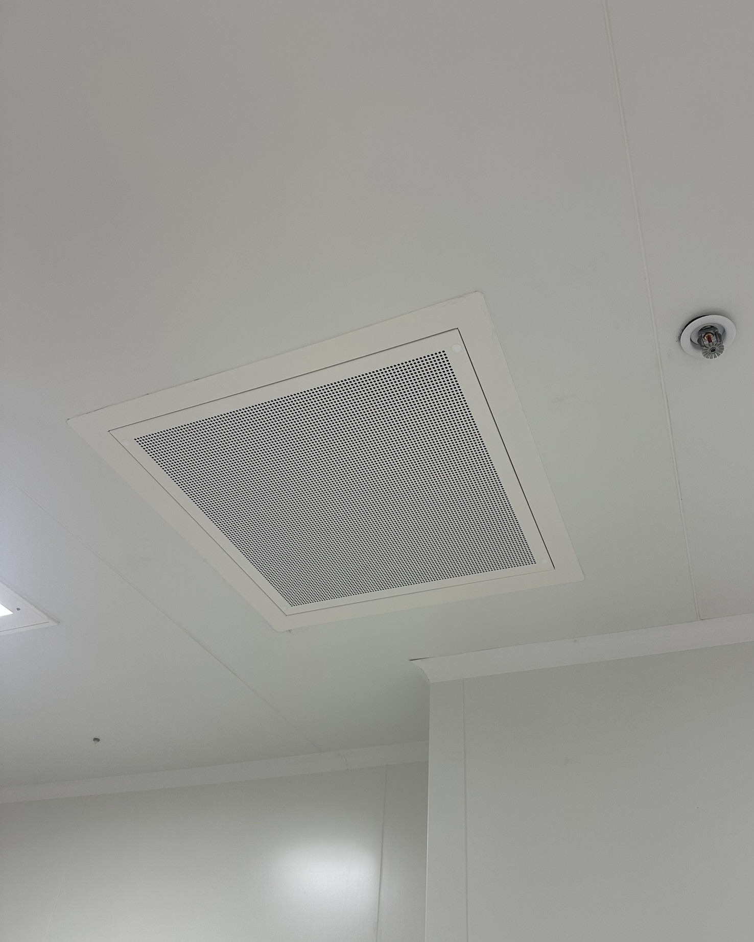 Diffuseur d'air perforé installé au plafond d'une salle propre, à proximité d'un sprinkler